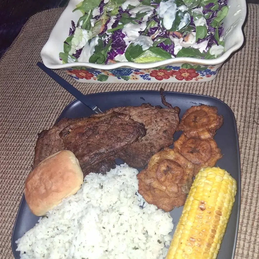Steak dinner with rice, corn, plantains, bread, and salad prepared by Karina